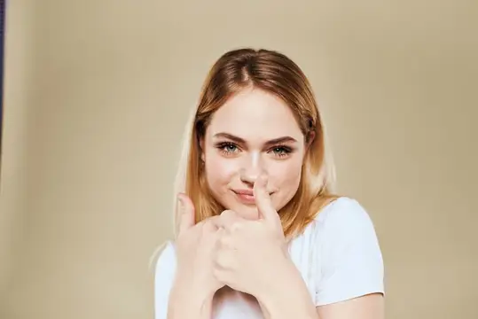 Весёлая женщина в белой футболке жестикулирует руками, выражая эмоции, на бежевом фоне
