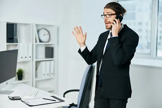 Мужчина в очках и костюме эмоционально говорит по телефону в офисе