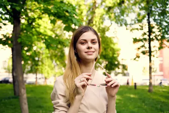 Молодая женщина с длинными волосами держит солнцезащитные очки в летнем парке