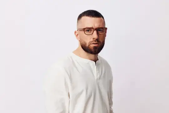 Бородатый мужчина в очках и белой рубашке на светлом фоне