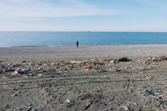 Одинокий человек стоит на пустынном пляже с мусором у моря