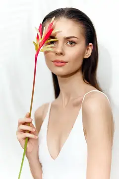 Молодая женщина с тропическим цветком у лица на белом фоне