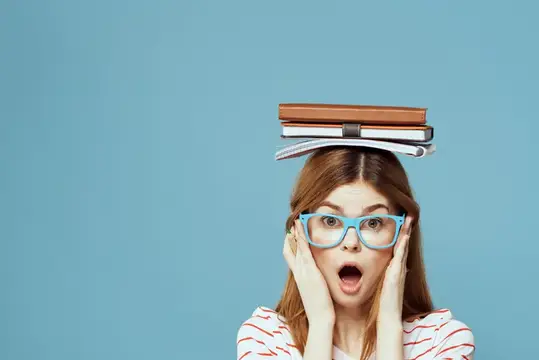 Студентка держит книги на голове на фоне синего цвета, что символизирует научное образование