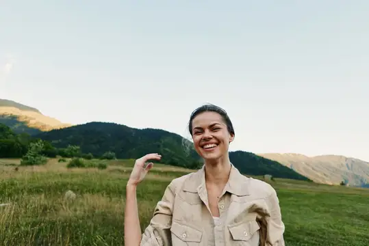 Улыбающаяся темноволосая женщина на фоне гор и луга
