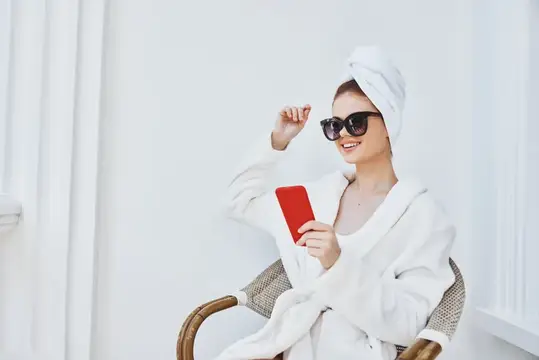 Весёлая женщина в солнцезащитных очках и халате на балконе с телефоном