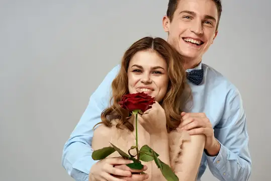 Улыбающийся парень обнимает девушку с красной розой