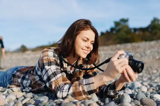 Улыбающаяся девушка лежит на каменистом пляже и фотографирует