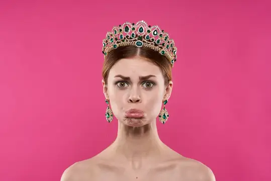 Недовольная женщина в роскошной короне на розовом фоне