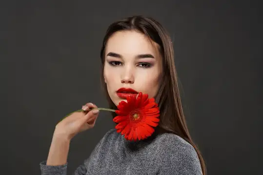 Брюнетка с красным цветком у лица, роскошная косметика, романтика