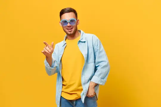 Улыбающийся парень в голубых очках показывает пальцем вверх на жёлтом фоне