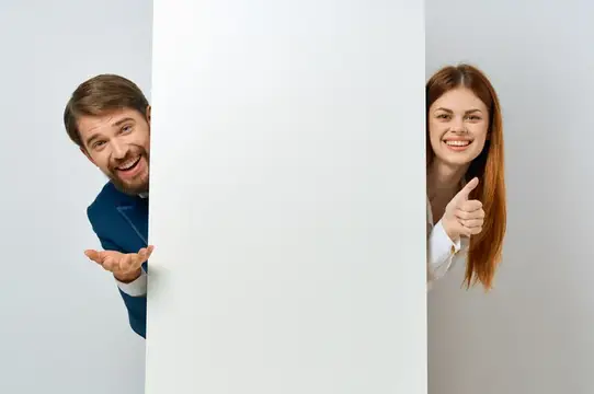 Улыбающиеся мужчина и женщина выглядывают из-за белой панели