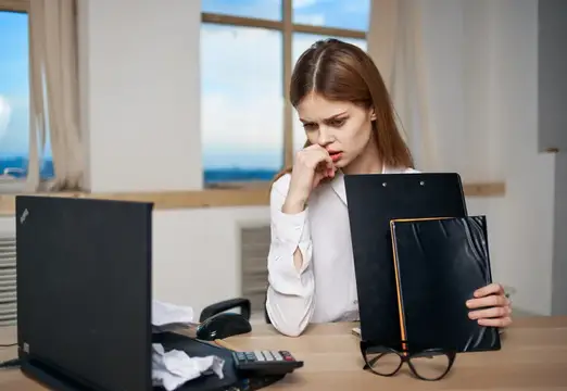 Задумчивая девушка с папками документов за рабочим столом в офисе