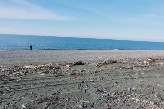 Мусор покрывает каменистый пляж, пока одинокая фигура смотрит на горизонт