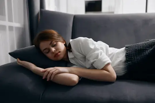 Женщина с закрытыми глазами отдыхает, лежа на диване