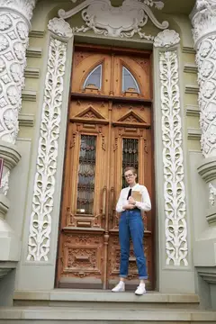 Девушка с книгой стоит на ступенях у резных деревянных дверей