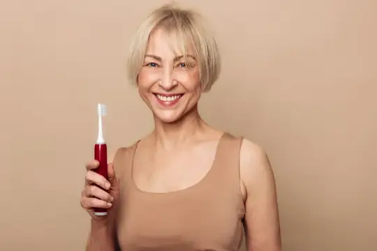 Улыбающаяся седовласая женщина с зубной щеткой в руке