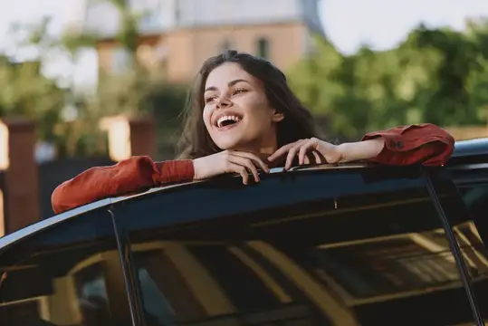 Смеющаяся темноволосая девушка выглядывает из люка автомобиля