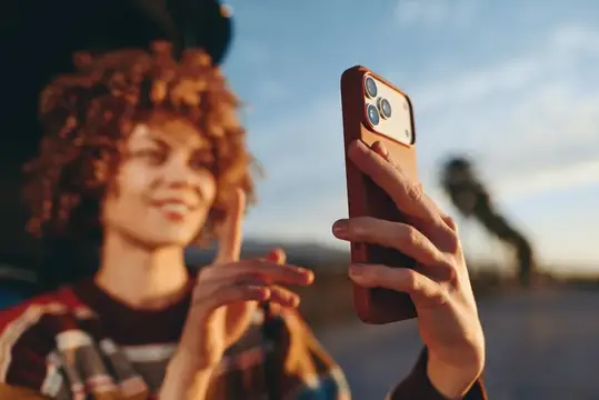 Рыжеволосая девушка смотрит в смартфон на закате