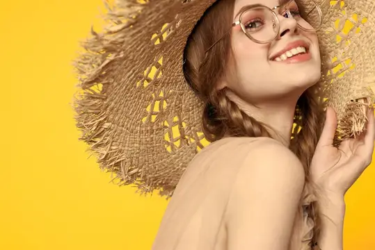Улыбающаяся девушка в соломенной шляпе и очках на жёлтом фоне