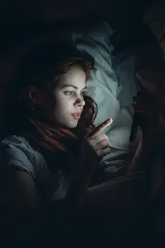 Девушка лежит в постели и смотрит на светящийся экран телефона
