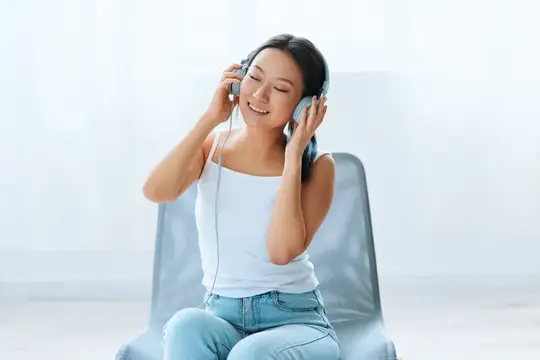 Улыбающаяся азиатская девушка слушает музыку в наушниках