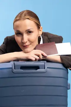 Молодая женщина с паспортом облокотилась на синий чемодан