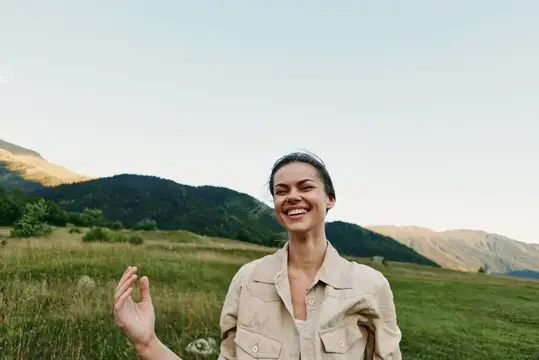 Улыбающаяся темноволосая женщина на фоне гор и луга