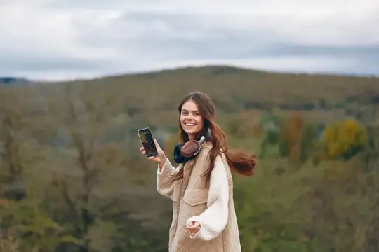 Улыбающаяся девушка с телефоном и наушниками на фоне осенних холмов