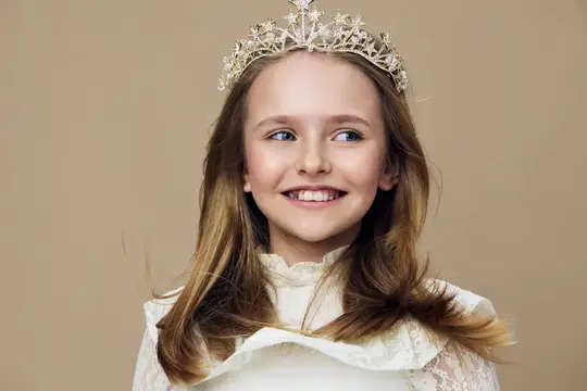 Улыбающаяся девочка в короне и белом платье