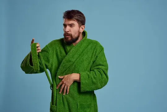 Бородатый мужчина в зелёном халате завязывает пояс на голубом фоне