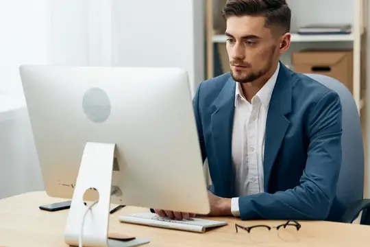 Молодой мужчина в синем пиджаке сосредоточенно работает за компьютером в офисе