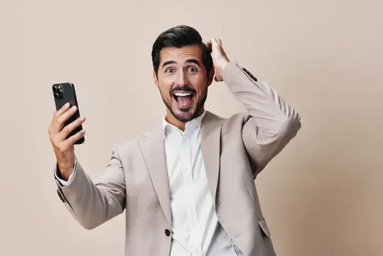 Мужчина в деловом костюме улыбается, держит смартфон на фоне бежевого пространства для копирования