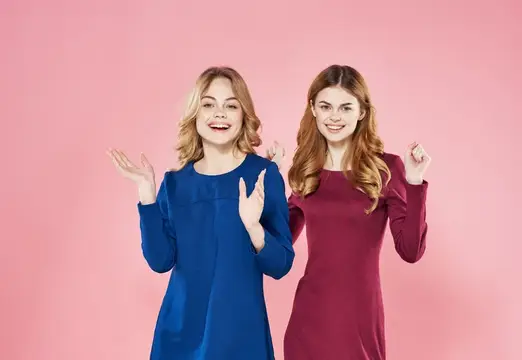 Две улыбающиеся девушки в синем и бордовом платьях на розовом фоне