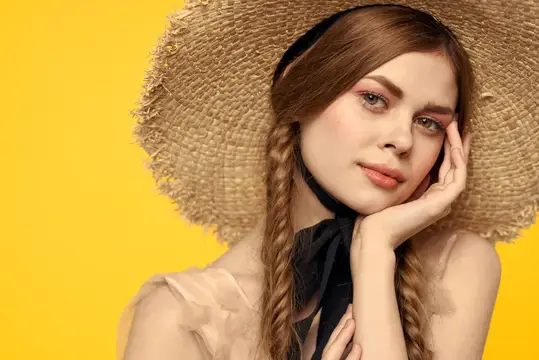 Молодая девушка в соломенной шляпе с косами на жёлтом фоне