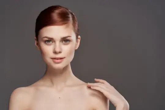 Рыжеволосая женщина с гладкой причёской на сером фоне