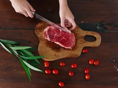 Руки нарезают кусок сырого мяса на деревянной доске
