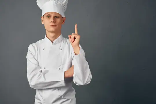 Мужчина в форме шеф-повара жестикулирует рукой, выражая эмоции, профессионально