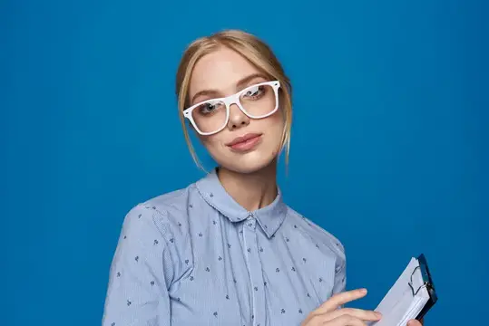 Светловолосая девушка в белых очках с блокнотом на синем фоне