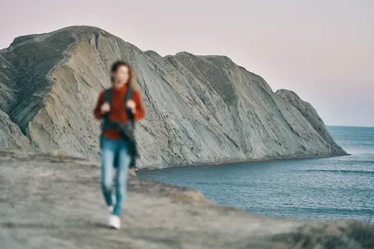 Размытая фигура бегущего мужчины на фоне скал и моря