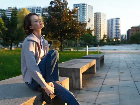 Молодая женщина с закрытыми глазами греется на солнце в городском парке
