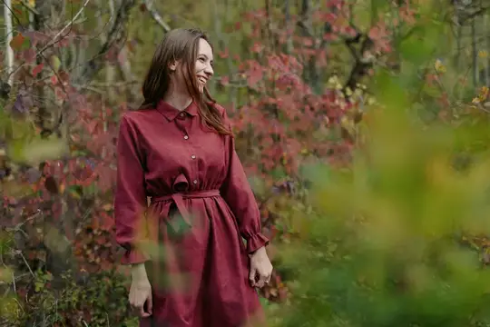 Улыбающаяся девушка в бордовом платье осенью в лесу