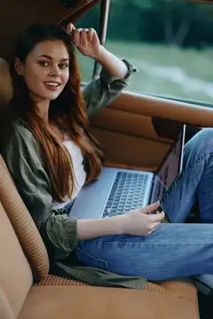 Улыбающаяся девушка с ноутбуком сидит в салоне автомобиля