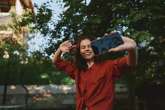 Улыбающаяся девушка в красной рубашке делает селфи на улице