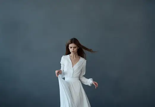 Молодая женщина в белом платье на сером фоне