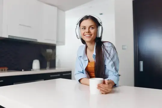 Молодая женщина наслаждается кофе и музыкой на кухне, надев наушники
