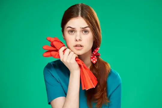 Удивлённая рыжеволосая девушка с красными резиновыми перчатками на зелёном фоне