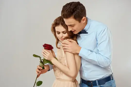 Молодой человек обнимает девушку с красной розой в руках