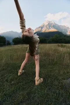 Молодая женщина танцует на лугу на фоне гор
