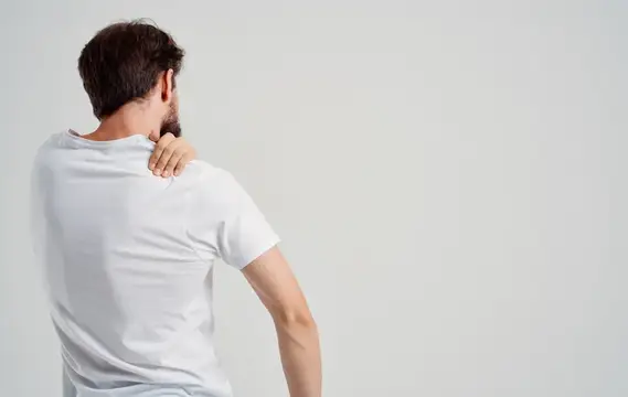 Мужчина в белой футболке массирует ноющее плечо
