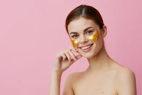Улыбающаяся девушка с золотыми патчами под глазами на розовом фоне